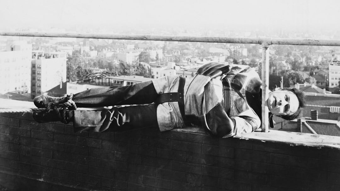 On a ledge about a city, Houdini holds on with his chin in a scene from the film ‘The Grim Game.’