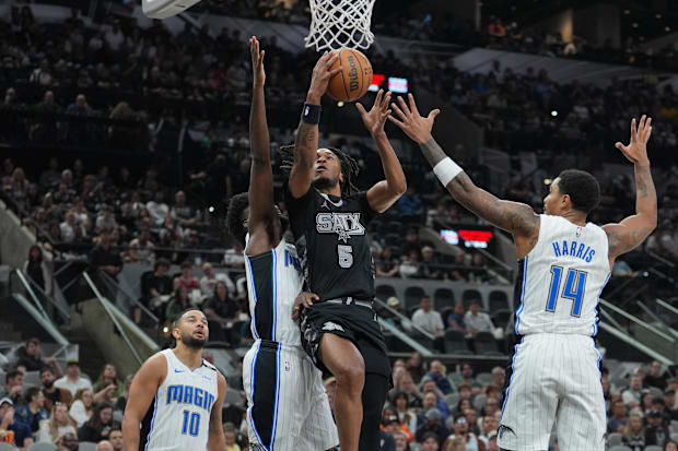 San Antonio Spurs guard Stephon Castle (5) goes up between Orlando Magic forward Jonathan Isaac (1) and guard Gary Harris (14