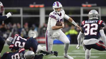 Bills quarterback Josh Allen (17) runs with the ball while evading tackles by New England Patriots defenders.