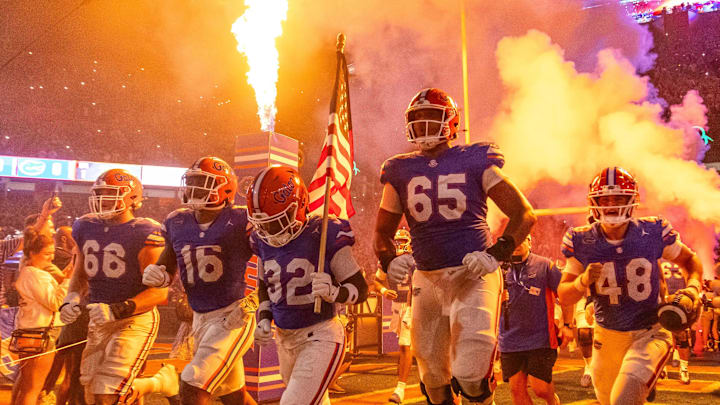 Florida Gators offensive lineman Brandon Crenshaw-Dickson (65) leaps in the air as Florida Gators defensive back Cahron Rackley (32) carries the American flag while running out of the tunnel with the team as fireworks and fire shoot out of towers before the start of the game at Ben Hill Griffin Stadium in Gainesville, FL on Saturday, October 5, 2024. [Doug Engle/Gainesville Sun]