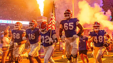 Florida Gators offensive lineman Brandon Crenshaw-Dickson (65) leaps in the air as Florida Gators defensive back Cahron Rackley (32) carries the American flag while running out of the tunnel with the team as fireworks and fire shoot out of towers before the start of the game at Ben Hill Griffin Stadium in Gainesville, FL on Saturday, October 5, 2024. [Doug Engle/Gainesville Sun]