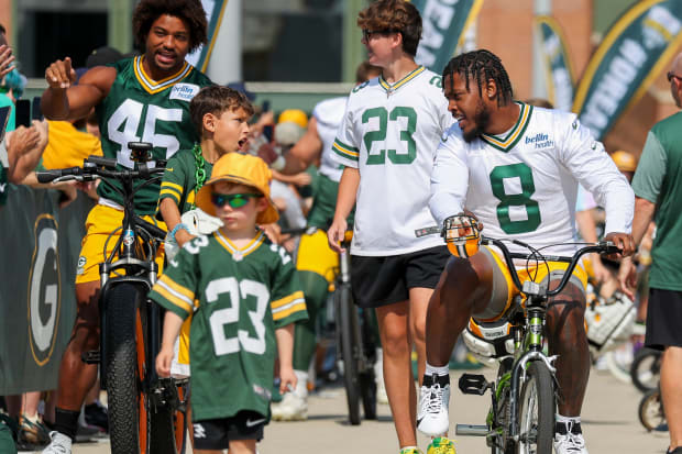 Green Bay Packers running back Josh Jacobs (8) talks with a young boy as he rides the boy's bicycle to practice.