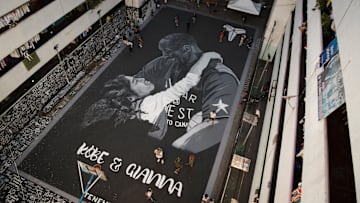 People walk beside a giant mural of Kobe and Gianna Bryant...