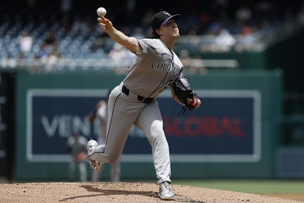 Dollander in a solid grey uniform throwing a ball against the Nationals in a black and purple hat out of a black glov