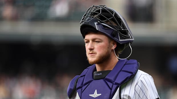 A baseball player in a purple and white uniform wearing a catcher's helmet on his head during a game.