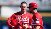 Cincinnati Reds outfielder Austin Hays (12), left, speaks with first base coach Collin Cowgill (54) in the first inning of a Cactus League game between the Cincinnati Reds and Cleveland Guardians, Saturday, Feb. 22, 2025, at the Goodyear Ballpark in Goodyear, Ariz.