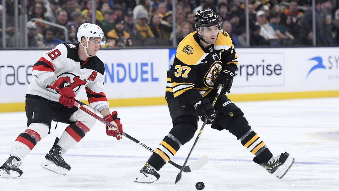 Apr 8, 2023; Boston, Massachusetts, USA;  Boston Bruins center Patrice Bergeron (37) controls the puck while New Jersey Devils left wing Ondrej Palat (18) defends during the third period at TD Garden. Mandatory Credit: Bob DeChiara-Imagn Images