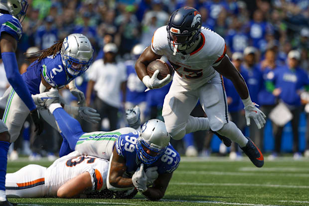 Denver Broncos running back Javonte Williams (33) breaks a tackle attempt by Seattle Seahawks defensive end Leonard Williams.