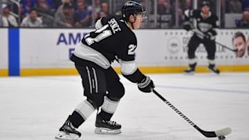 Mar 25, 2025; Los Angeles, California, USA; Los Angeles Kings defenseman Jordan Spence (21) controls the puck against the New York Rangers during the first period at Crypto.com Arena. Mandatory Credit: Gary A. Vasquez-Imagn Images