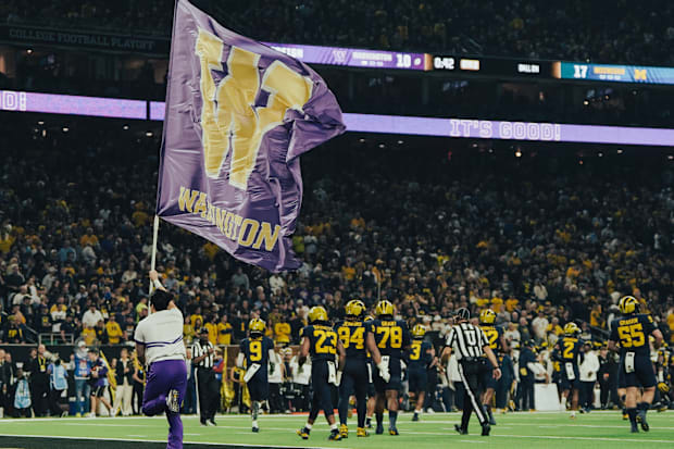 A flag-bearing Husky cheerleader runs past the Michigan football team at NRG Stadium in Houston.