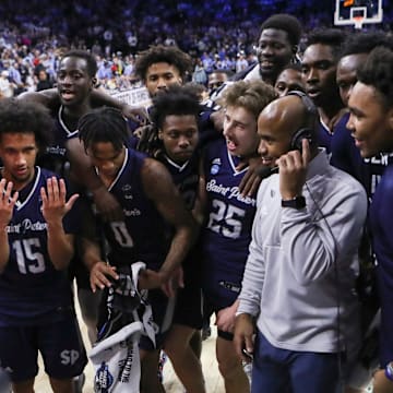 Saint Peter's players celebrate around head coach Shaheen Holloway as he does a television interview after the Peacocks' 67-64 win against Purdue to advance to the Elite Eight in the NCAA tournament at the Wells Fargo Center in Philadelphia, March 25, 2022.
