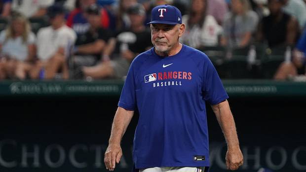 O gerente do Texas Rangers, Bruce Bochy, caminha até o monte enquanto usava uma camiseta azul com Rangers na frente.