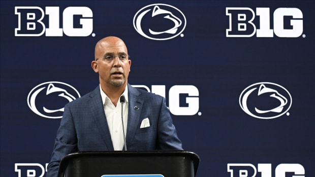 Penn State football coach speaks from behind a podium with the Big Ten and Nittany Lions logo behind him.