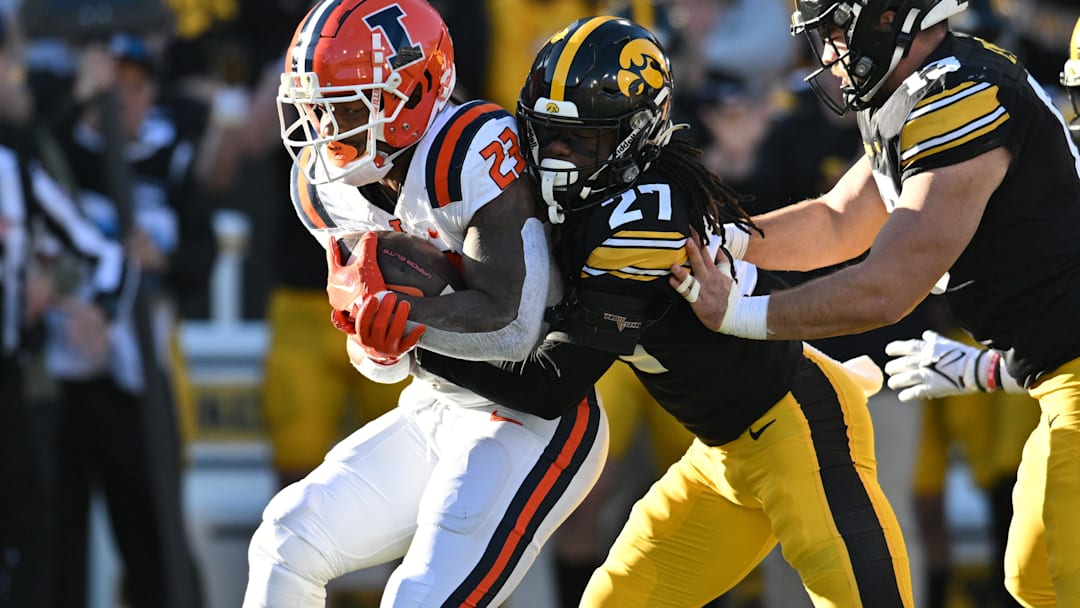 Nov 18, 2023; Iowa City, Iowa, USA; Illinois Fighting Illini running back Reggie Love III (23) is stopped by Iowa Hawkeyes defensive back Jermari Harris (27) and defensive end Joe Evans (13) during the first quarter at Kinnick Stadium. Mandatory Credit: Jeffrey Becker-USA TODAY Sports