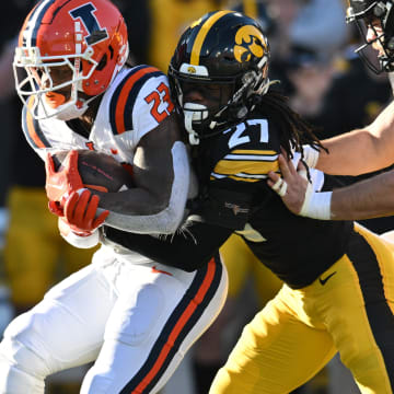 Nov 18, 2023; Iowa City, Iowa, USA; Illinois Fighting Illini running back Reggie Love III (23) is stopped by Iowa Hawkeyes defensive back Jermari Harris (27) and defensive end Joe Evans (13) during the first quarter at Kinnick Stadium. Mandatory Credit: Jeffrey Becker-USA TODAY Sports