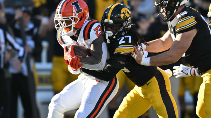 Nov 18, 2023; Iowa City, Iowa, USA; Illinois Fighting Illini running back Reggie Love III (23) is stopped by Iowa Hawkeyes defensive back Jermari Harris (27) and defensive end Joe Evans (13) during the first quarter at Kinnick Stadium. Mandatory Credit: Jeffrey Becker-USA TODAY Sports