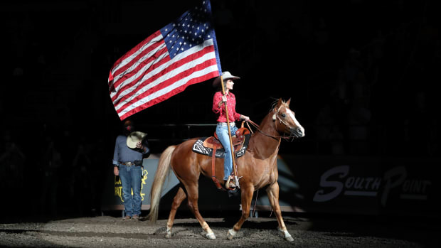 A lady on a red horse carrying the American flag horseback into the arena.