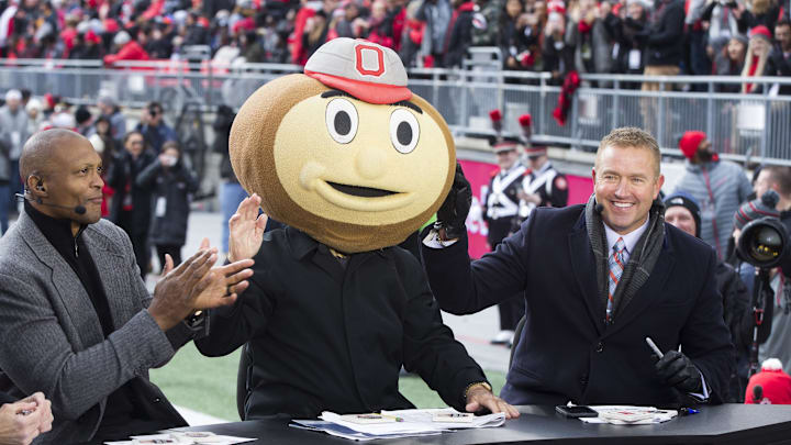 ESPN College Gameday host Lee Corso puts on a Brutus Buckeye head on while sitting between former Buckeyes Eddie George and Kirk Herbstreit before a November 2019 game between the Ohio State Buckeyes and Penn State Nittany Lions at Ohio Stadium. 