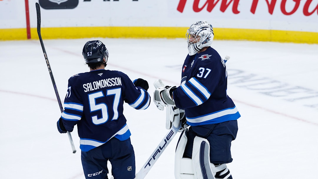 Oct 2, 2024; Winnipeg, Manitoba, CAN;  Winnipeg Jets goalie Connor Hellebuyck (37) is congratulated by Winnipeg Jets defenseman Elias Salomonsson (57) on his win against the Calgary Flames at the end of the third period at Canada Life Centre. Mandatory Credit: Terrence Lee-Imagn Images