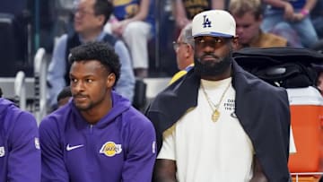 Oct 5, 2025; San Francisco, California, USA;   Los Angeles Lakers guard Bronny James (9) and forward LeBron James (23), wearing a Los Angeles Dodgers cap, watch the action against the Golden State Warriors in the first quarter at Chase Center. Mandatory Credit: David Gonzales-Imagn Images
