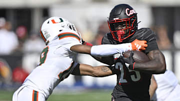 Oct 19, 2024; Louisville, Kentucky, USA; Louisville Cardinals running back Isaac Brown (25) runs the ball against Miami Hurricanes defensive back D'Yoni Hill (19) during the first half at L&N Federal Credit Union Stadium. Mandatory Credit: Jamie Rhodes-Imagn Images