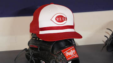 Cincinnati Reds hat and glove rest on the bench in the dugout