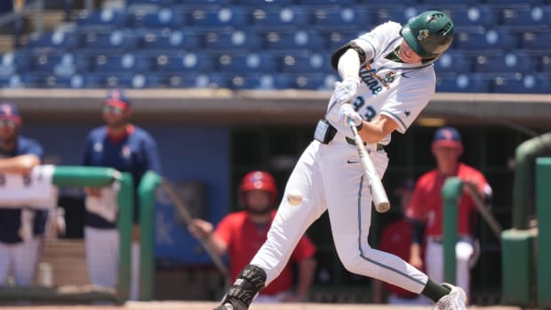 A baseball player in a white uniform swings a bat.