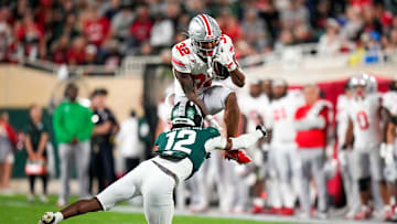Sep 28, 2024; East Lansing, Michigan, USA; Ohio State Buckeyes running back TreVeyon Henderson (32) hurdles over Michigan State Spartans defensive back Justin Denson Jr. (12) in the second half at Spartan Stadium on Saturday.