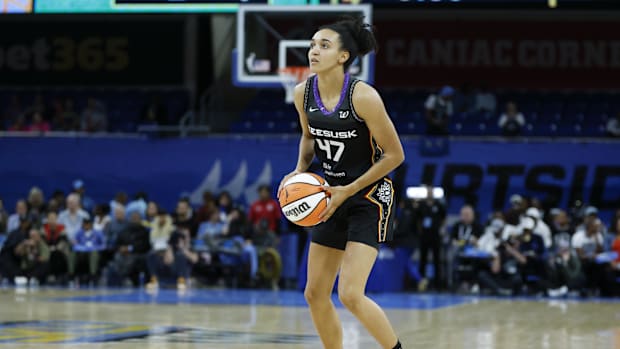 A female basketball player wearing a black uniform on the court while holding a white and orange basketball