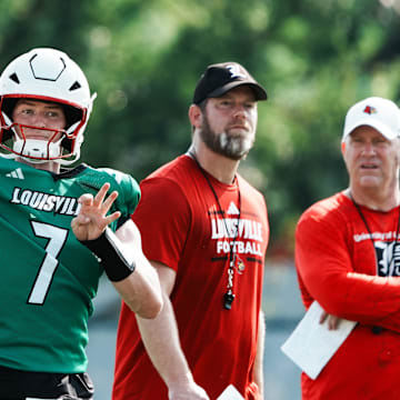 U of L QB Miller Moss (7) passes during practice as OC Brian Brohm and head coach Jeff Brohm, right, watch on the practice field at Cardinal Stadium in Louisville, Ky. on July 30, 2025.