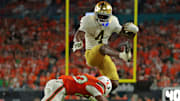 Notre Dame Fighting Irish running back Jeremiyah Love hurdles over Miami Hurricanes defensive back Dylan Day