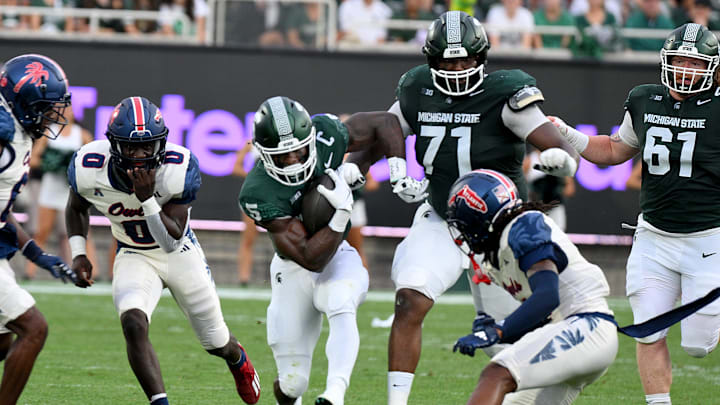 Aug 30, 2024; East Lansing, Michigan, USA;  Michigan State Spartans running back Nate Carter (5) squeezes through a hole during the game against the Florida Atlantic Owls at Spartan Stadium. Mandatory Credit: Dale Young-Imagn Images
