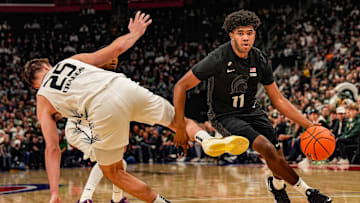 Michigan State Spartans guard Jase Richardson (11) dribbles past Oakland Golden Grizzlies forward Cooper Craggs (25) after he loses his balance during the first period at Little Caesars Arena in Detroit on Tuesday, Dec. 17, 2024.