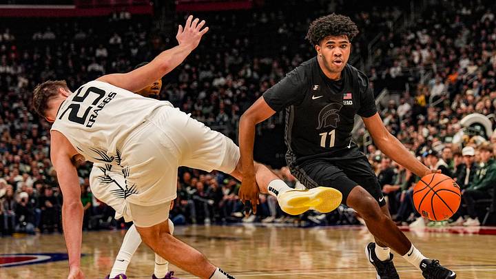 Michigan State Spartans guard Jase Richardson (11) dribbles past Oakland Golden Grizzlies forward Cooper Craggs (25) after he loses his balance during the first period at Little Caesars Arena in Detroit on Tuesday, Dec. 17, 2024.
