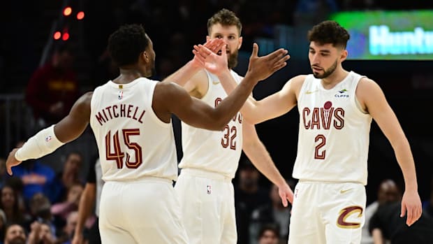 Three basketball players celebrating while wearing white uniforms.