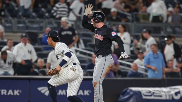 A baseball player wearing a navy jersey, gray pants, and a navy helmet while celebrating a hit.