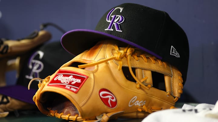 A detailed view of a Colorado Rockies hat and glove on the bench of a dugout.