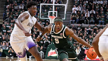Jan 9, 2025; East Lansing, Michigan, USA;  Michigan State Spartans guard Tre Holloman (5) drives past Washington Huskies forward Great Osobor (1) during the second half at Jack Breslin Student Events Center. Mandatory Credit: Dale Young-Imagn Images