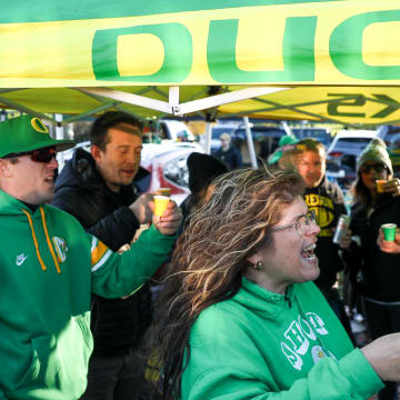 Denyse Renner, center, takes shots with other Oregon fans as they tailgate before the annual rivalry game on Friday, Nov. 24, 2023 at Autzen Stadium in Eugene, Ore.