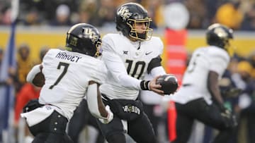 Nov 23, 2024; Morgantown, West Virginia, USA; UCF Knights quarterback Dylan Rizk (10) hands the ball off to running back RJ Harvey (7) against the West Virginia Mountaineers during the first quarter at Mountaineer Field at Milan Puskar Stadium. Mandatory Credit: Ben Queen-Imagn Images
