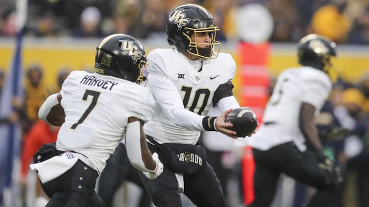 Nov 23, 2024; Morgantown, West Virginia, USA; UCF Knights quarterback Dylan Rizk (10) hands the ball off to running back RJ Harvey (7) against the West Virginia Mountaineers during the first quarter at Mountaineer Field at Milan Puskar Stadium. Mandatory Credit: Ben Queen-Imagn Images