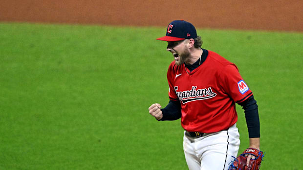 A baseball player yelling while wearing a red jersey, white pants, a navy and red hat, and a red and blue baseball glove.