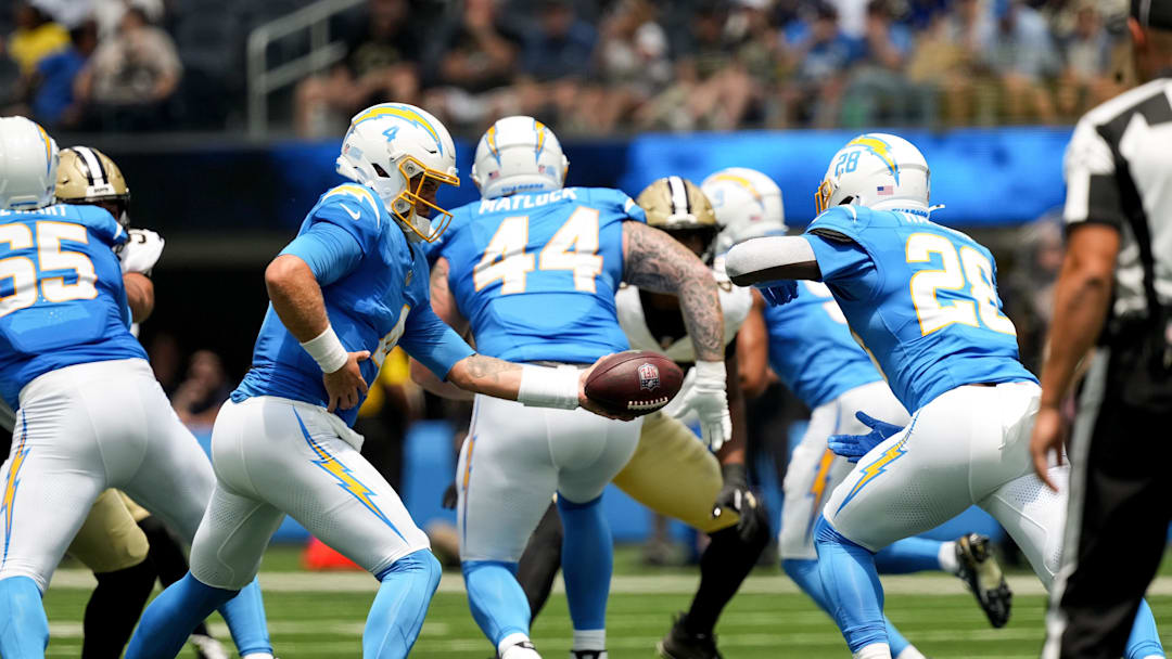 Aug 10, 2025; Inglewood, California, USA; Los Angeles Chargers quarterback Taylor Heinicke (4) hands off to running back Hassan Haskins (28) against the New Orleans Saints at SoFi Stadium. 