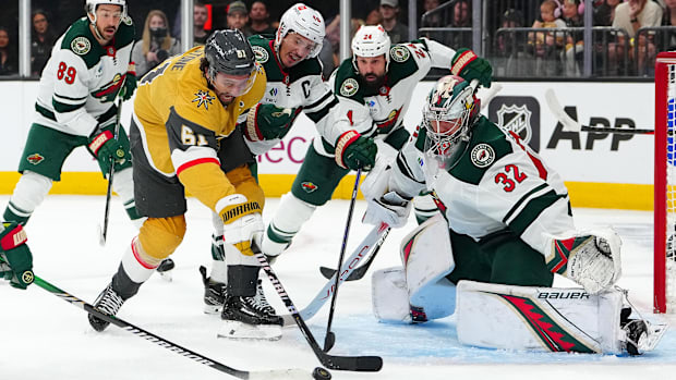 Hockey goalie in white uniform attempts stick check on forward in gold uniform