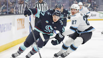 Dec 30, 2024; Seattle, Washington, USA; Seattle Kraken center Yanni Gourde (37) skates with the puck ahead of Utah Hockey Club center Barrett Hayton (27) during the first period at Climate Pledge Arena. Mandatory Credit: Joe Nicholson-Imagn Images