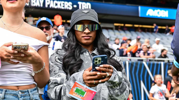 Aug 17, 2024; Chicago, Illinois, USA; United States gymnast Simone Biles, right, stands on the sideline before the game between the Chicago Bears and the Cincinnati Bengals at Soldier Field.