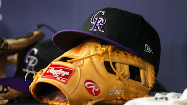 A black and purple Colorado Rockies hat sits on top of a light brown fielding glove in the dugout. 
