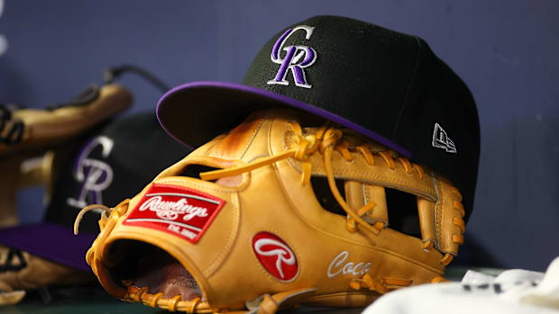 Black Colorado Rockies Hat with purple brim sitting on top of a glove in the dugout.