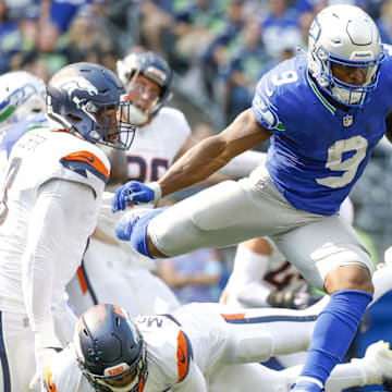 Sep 8, 2024; Seattle, Washington, USA; Seattle Seahawks running back Kenneth Walker III (9) jumps over a tackle attempt by Denver Broncos cornerback JaQuan McMillian (29) during the second quarter at Lumen Field.