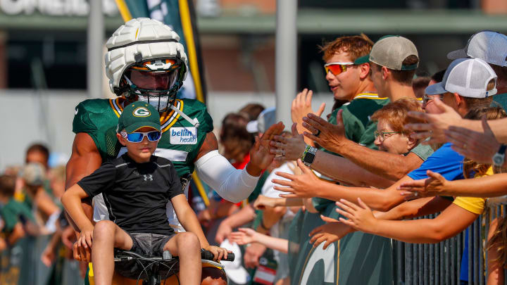 A young Green Bay Packers fan rides on the handlebars of his bicycle while riding to practice with Eric Wilson.